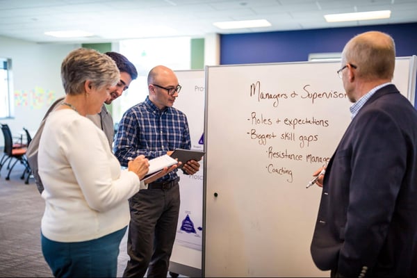 A-group-of-employees-collaborating-using-a-whiteboard-symbolizing-teamwork-and-problem-solving-in-Six-Sigma-initiatives.